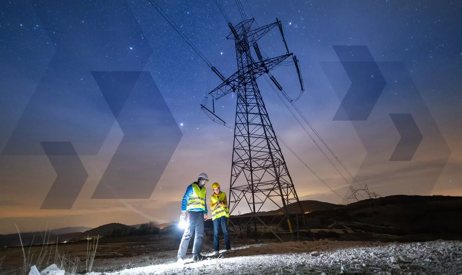 Two utility engineers inspect a high-voltage transmission tower at night